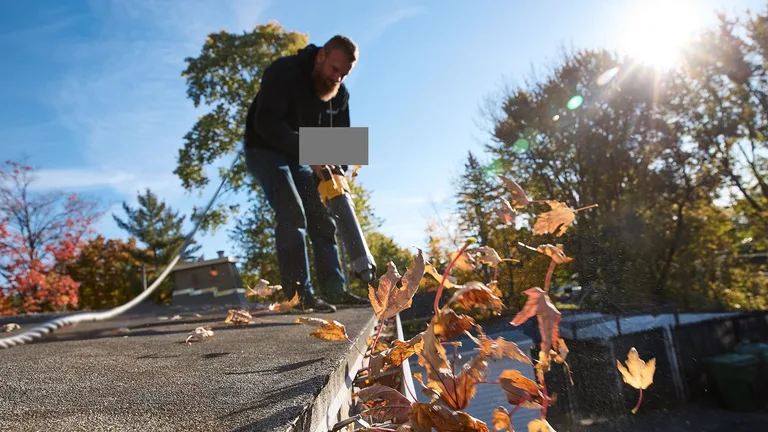 Technician clearing autumn leaves from an eavestrough